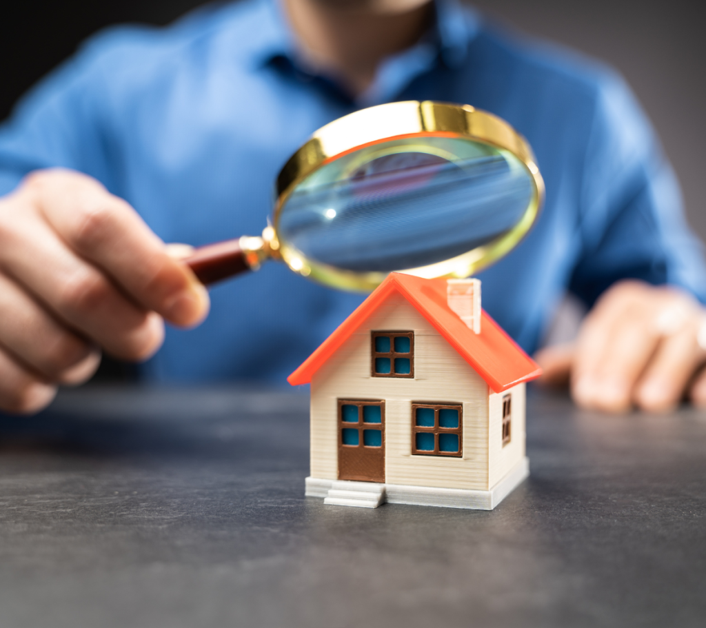Person inspecting a small house model with a magnifying glass.
