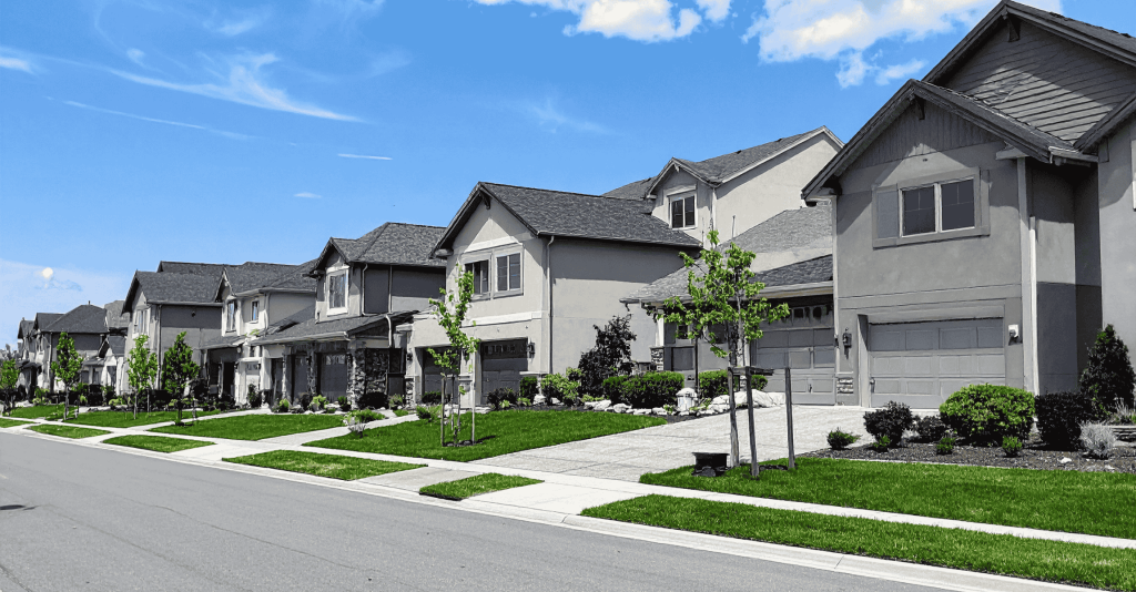 Row of modern suburban houses with green lawns under a bright blue sky.