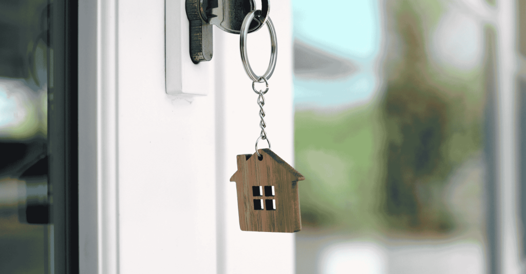 House-shaped keychain hanging from a key in a front door, symbolizing homeownership and real estate.