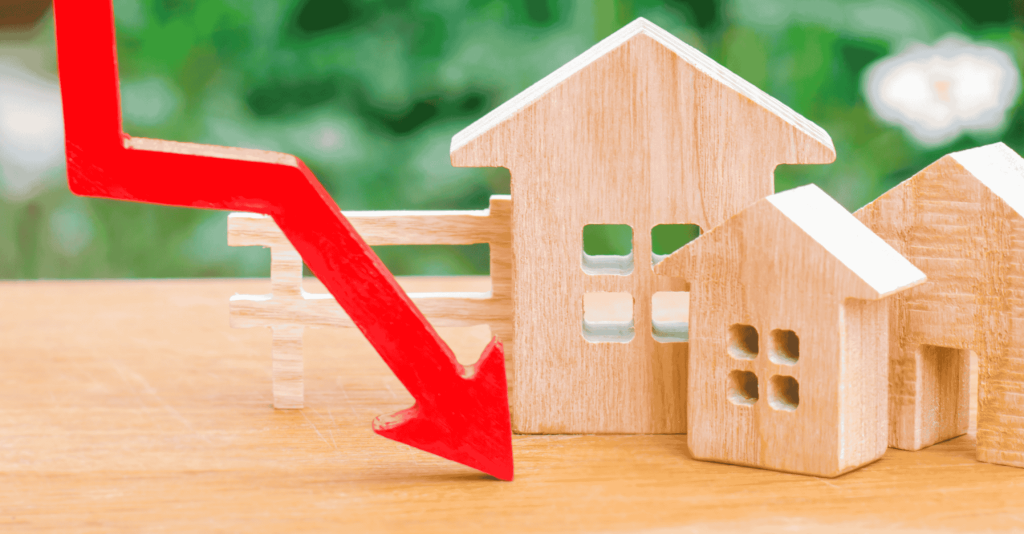 Wooden house models with a red downward arrow symbolizing falling home prices or declining real estate market.
