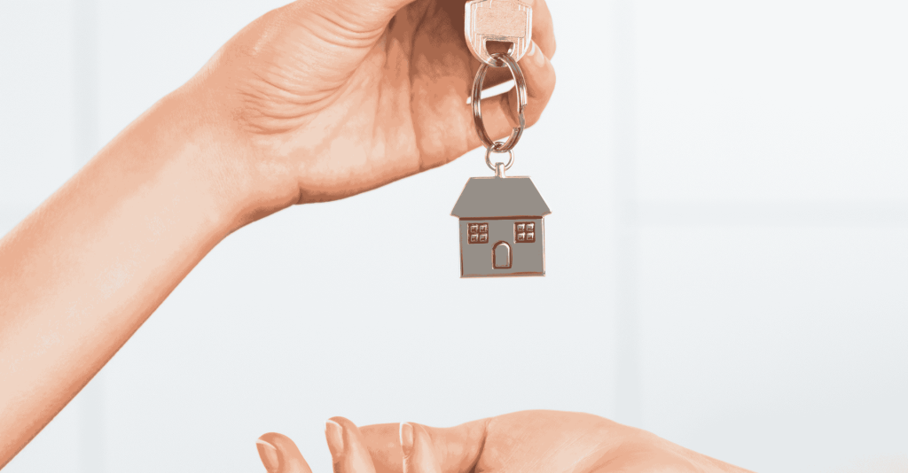 Hand holding a house-shaped keychain, symbolizing buying or selling a home.