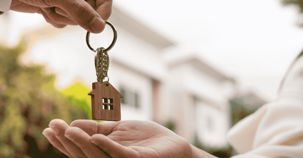 Person handing over house-shaped keychain to another person, symbolizing a home sale or purchase.