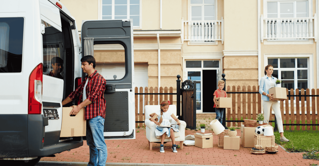 Family moving out of their home; a man loads boxes into a moving van while a woman and two children carry and organize items outside the house.