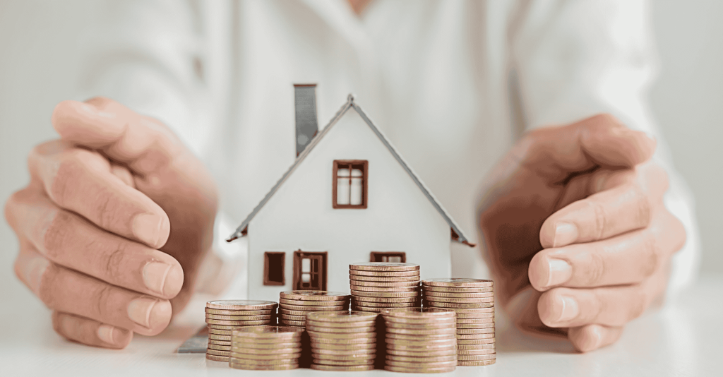 Hands protecting a small house model with stacks of coins in front, symbolizing home investment or earnest money deposit.