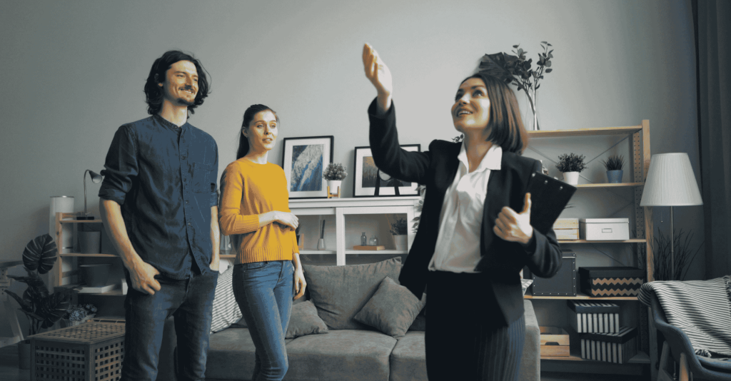 Real estate agent showing a modern living room to a smiling couple during a home tour.