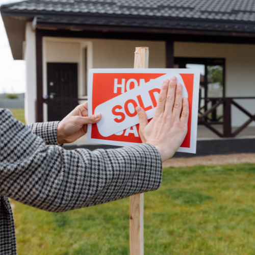 A seller placing a “SOLD” sticker on a for sale sign in front of a Florida home, symbolizing a successful sale without a realtor.