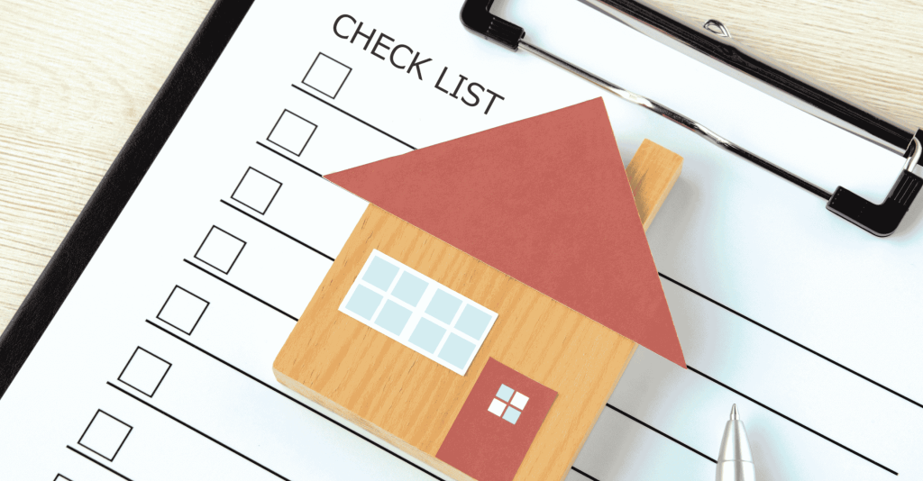 House-shaped model placed on top of a checklist clipboard with a pen beside it, symbolizing home-selling preparation tasks.