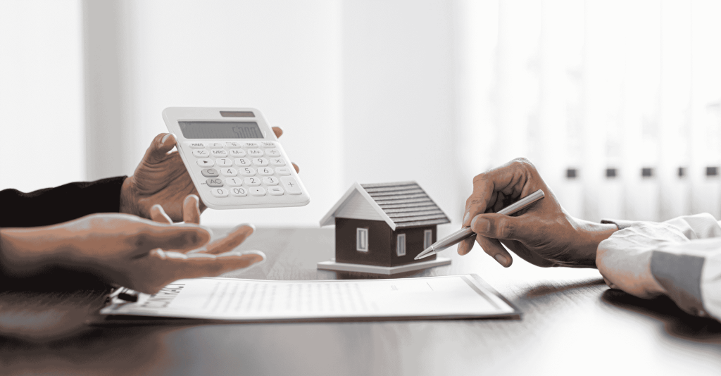 Two people reviewing home sale documents with a small house model, calculator, and pen on the table, discussing property disclosures and financial details.